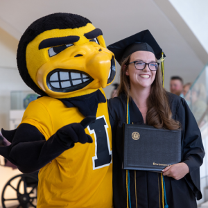 Carver College of Medicine graduate standing next to mascot Herky the Hawk